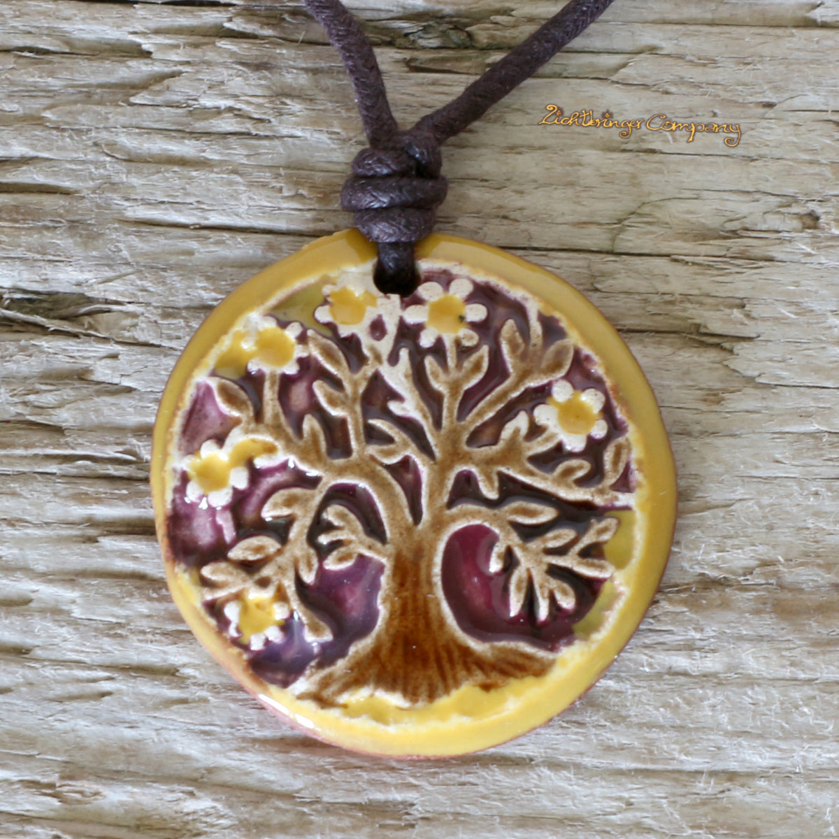 Lebensbaum-Anhänger aus Ton in Gelb, an gewachster Baumwollkette – handgefertigtes Keramik-Amulett. Brauner Baum vor violettem Hintergrund, mit gelbem Rand und Blüten.