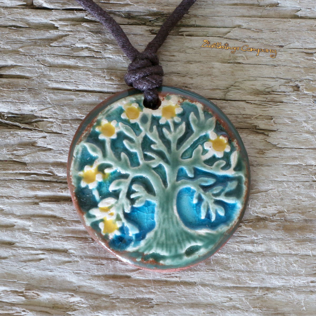 Lebensbaum-Anhänger aus Ton in Grün-Blau, an gewachster Baumwollkette – handgefertigtes Keramik-Amulett. Grüner Baum mit gelben Blüten auf türkisem Hintergrund.