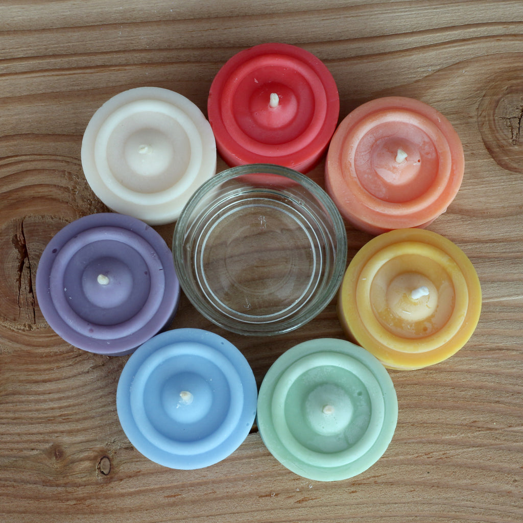 7 Teelichte in 7 Farben, plus ein Teelichtglas