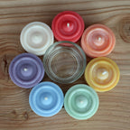 7 Teelichte in 7 Farben, plus ein Teelichtglas